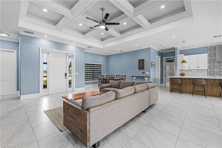 Living area with coffered ceiling, crown molding, beamed ceiling, ceiling fan, and light flooring