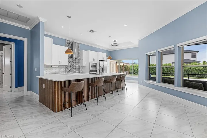 Kitchen featuring a kitchen breakfast bar, white cabinets, recessed lighting, hanging light fixtures, and wall chimney exhaust hood