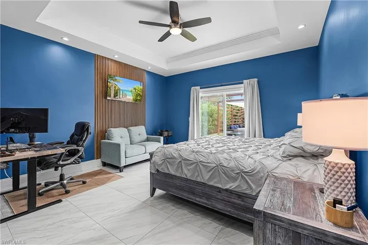 Primary bedroom with access to outside, a ceiling fan, light flooring, and a tray ceiling