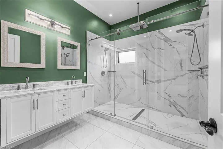 Primary bathroom with double vanity, a marble finish shower, and light floors