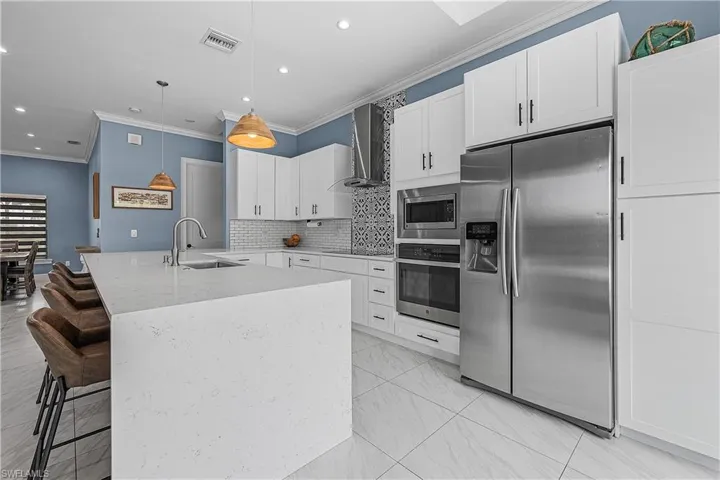 Kitchen featuring stainless steel appliances, a kitchen bar, white cabinets, and wall chimney range hood
