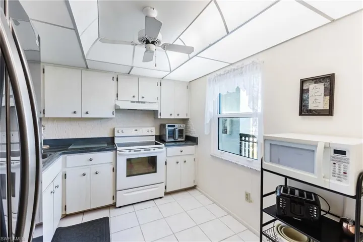 Kitchen with white appliances, dark countertops, tasteful backsplash, light tile patterned floors, and white cabinets