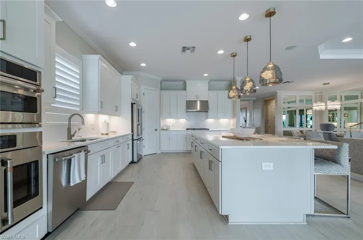 Kitchen featuring crown molding, stainless steel appliances, white cabinets, light stone counters, and hanging light fixtures