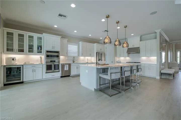 Kitchen featuring crown molding, a kitchen bar, wine cooler, white cabinets, and decorative backsplash
