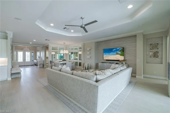 Living area featuring a tray ceiling, light wood-style flooring, ornamental molding, a ceiling fan, and recessed lighting