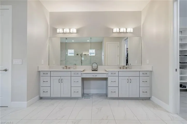 Full bath featuring a marble finish shower, double vanity, a walk in closet, and light marble finish flooring
