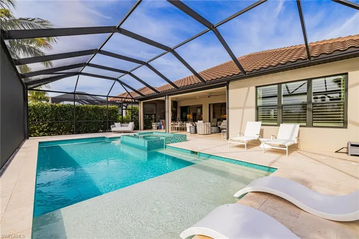 View of pool featuring a sunroom, a patio, a pool with connected hot tub, and glass enclosure
