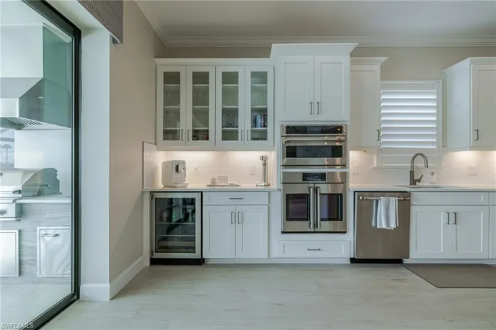 Kitchen featuring white cabinetry, stainless steel appliances, wine cooler, light stone countertops, and glass insert cabinets