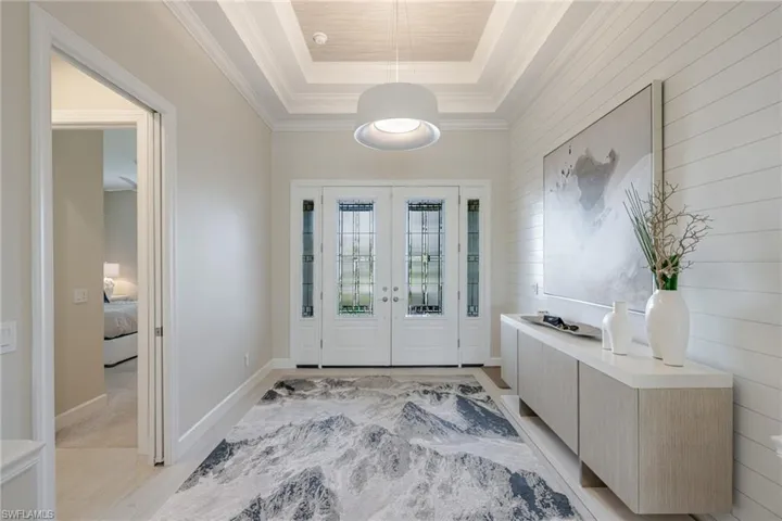Foyer featuring french doors, wood walls, a tray ceiling, and crown molding