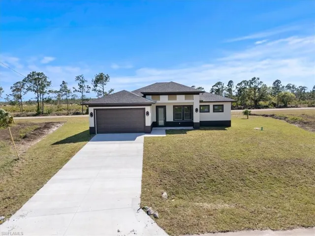 Prairie-style home with a garage, stucco siding, concrete driveway, and a front lawn