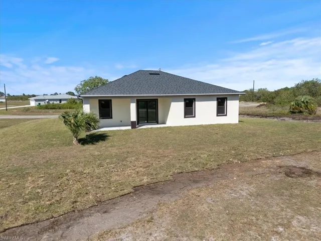 Back of property with stucco siding, a lawn, and a shingled roof
