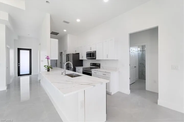 Kitchen featuring visible vents, a peninsula, stainless steel appliances, white cabinetry, and a sink