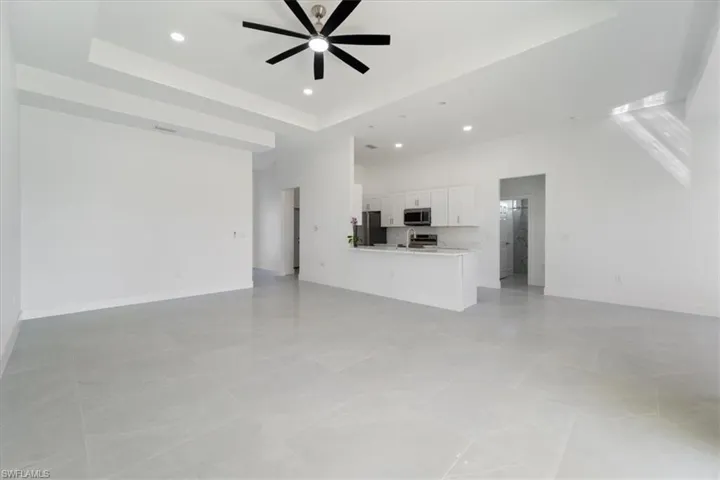 Unfurnished living room with a ceiling fan, baseboards, a tray ceiling, recessed lighting, and a towering ceiling