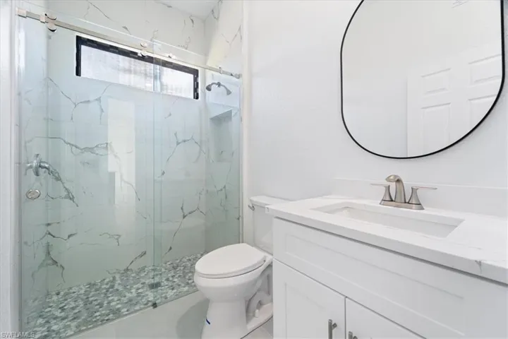 Full bathroom featuring a marble finish shower, toilet, and vanity