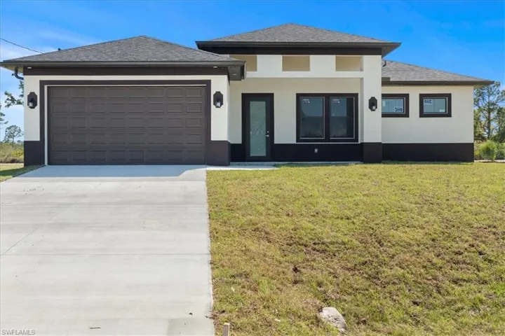 Prairie-style house with stucco siding, a garage, concrete driveway, and a front lawn