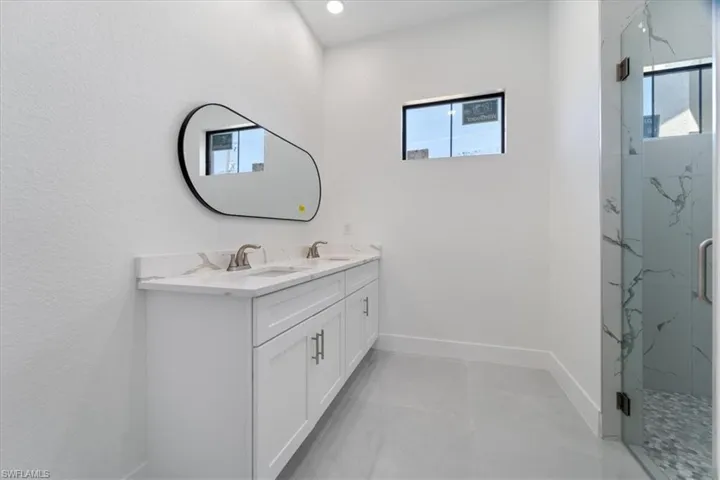 Bathroom featuring double vanity, baseboards, a marble finish shower, and a sink