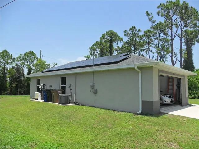 View of home's exterior with stucco siding, a yard, solar panels, driveway, and a shingled roof