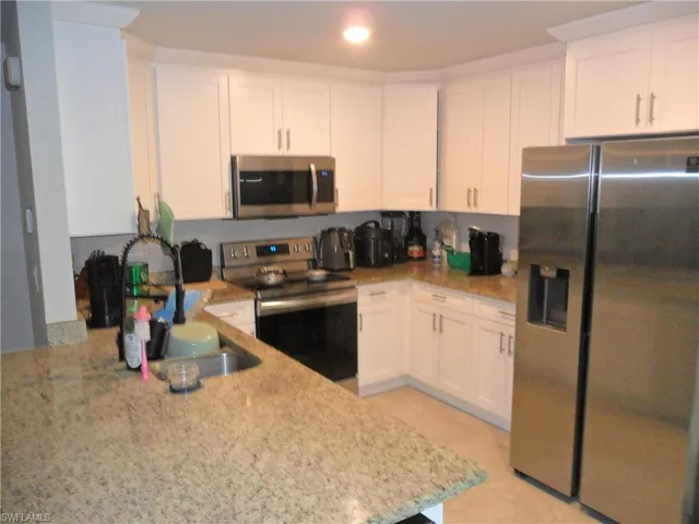 Kitchen with stainless steel appliances, light stone countertops, white cabinets, and recessed lighting