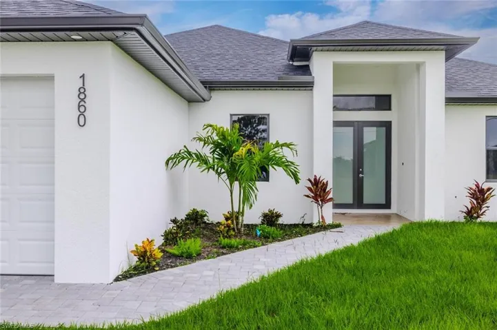 Doorway to property featuring a shingled roof, stucco siding, a lawn, an attached garage, and french doors