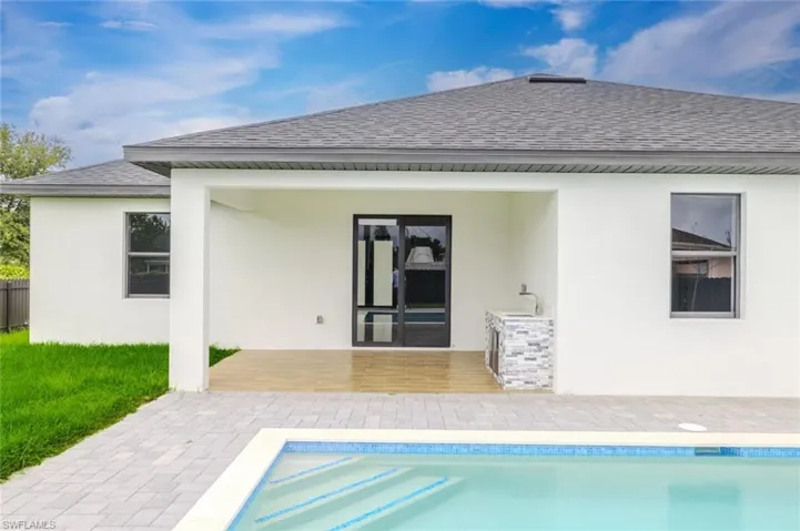 Back of property with roof with shingles, a patio, an outdoor pool, and stucco siding