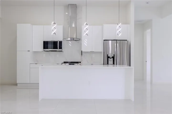 Kitchen with white cabinets, modern cabinets, backsplash, and wall chimney range hood