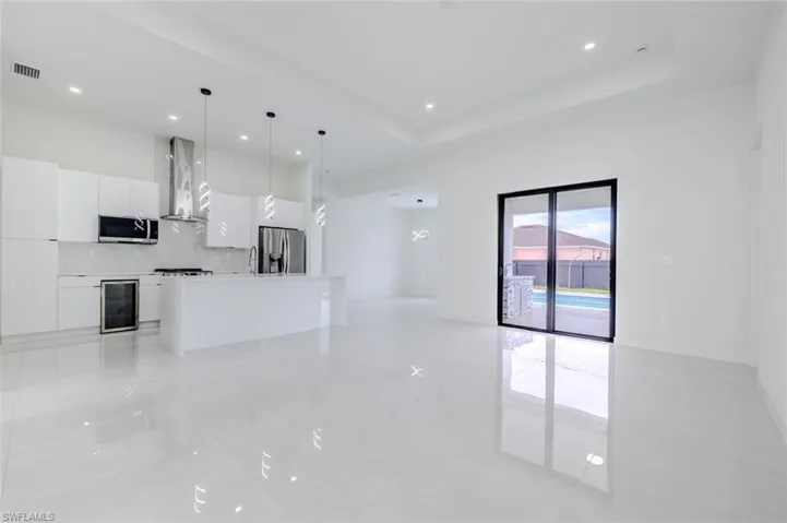 Unfurnished living room featuring recessed lighting, wine cooler, a tray ceiling, and light tile patterned floors