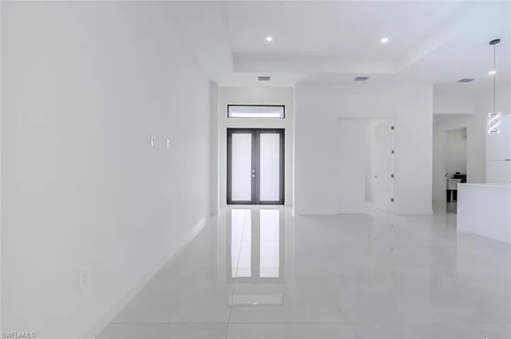 Empty room featuring a raised ceiling, light tile patterned flooring, french doors, and recessed lighting