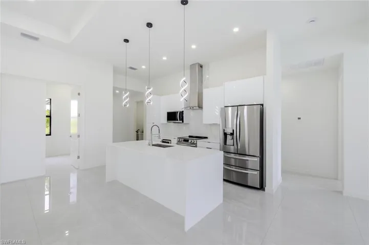 Kitchen featuring pendant lighting, stainless steel appliances, an island with sink, white cabinetry, and wall chimney exhaust hood