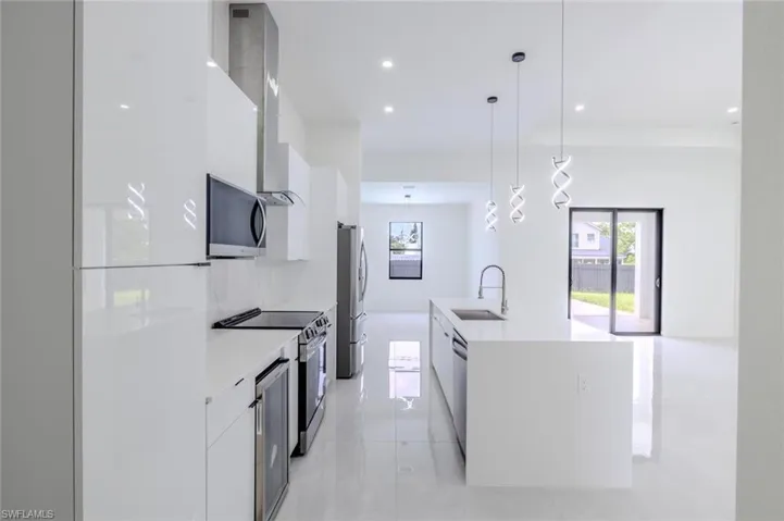 Kitchen with modern cabinets, white cabinets, hanging light fixtures, appliances with stainless steel finishes, and light stone countertops