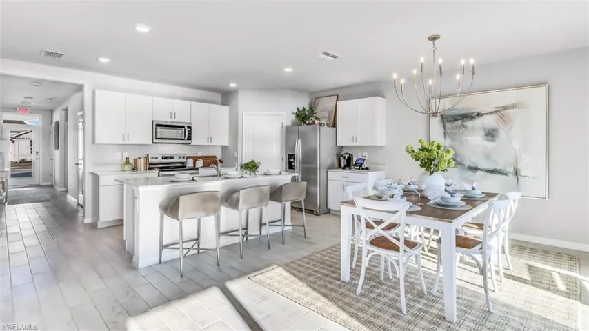 Model home. Kitchen with white cabinets, stainless steel appliances, a chandelier, a kitchen bar, and a center island with sink