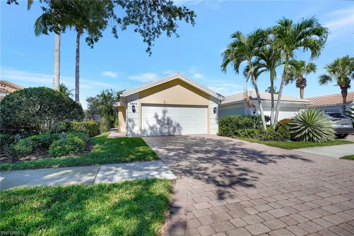 Exterior featuring a two-car garage, stucco finish, paver driveway, and mature tropical landscaping