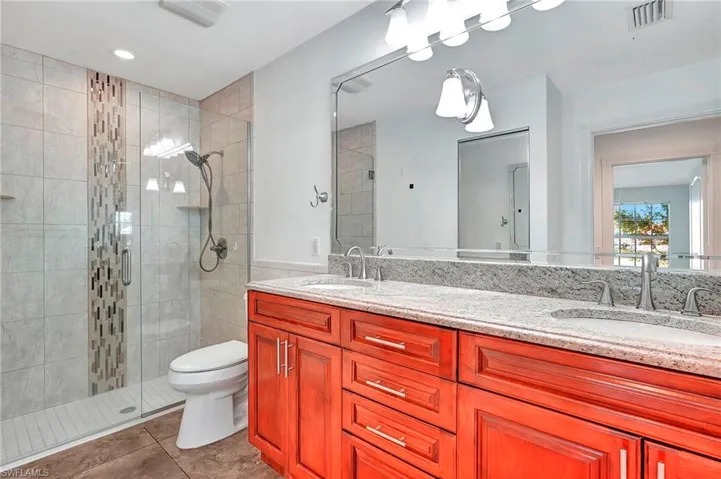 Bathroom featuring a dual-sink vanity with a light-toned countertop, a large frameless mirror, and a walk-in shower with a glass enclosure and decorative tile accent