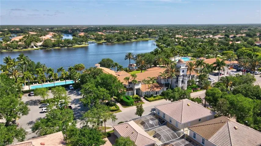 Expansive lake views bordering a community building with a tile roof, surrounded by mature palm trees and lush landscaping