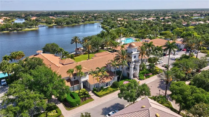 Expansive water feature bordering a property with terracotta-tiled roofs, a large exterior pool, and abundant mature palm trees