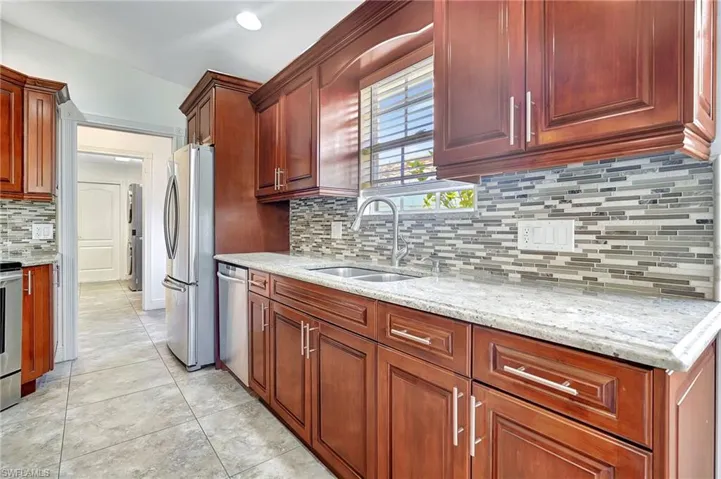 Kitchen featuring rich wood cabinetry, stone countertops, a mosaic tile backsplash, stainless steel appliances, and tile flooring