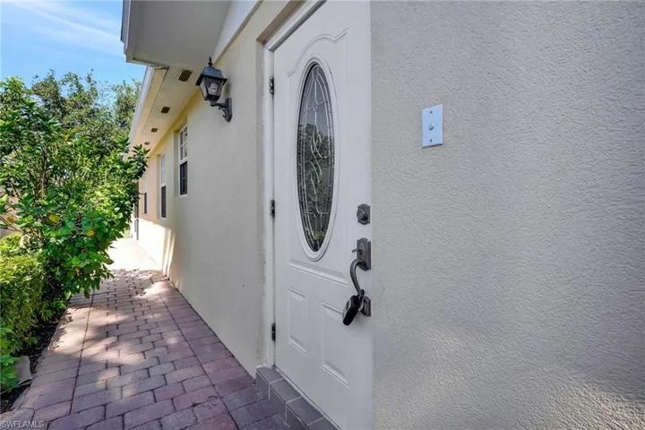 White entry door with decorative oval glass insert, textured stucco exterior, and a paver walkway