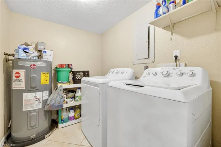 Washroom with washer and dryer, light tile patterned floors, electric water heater, and a textured ceiling