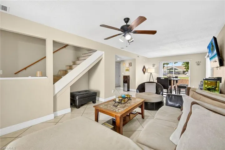 Living area featuring a ceiling fan, stairway, and light tile patterned floors