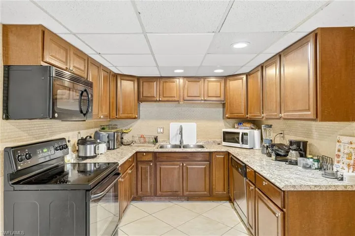 Kitchen featuring black appliances, a drop ceiling, brown cabinets, light countertops, and light tile patterned flooring