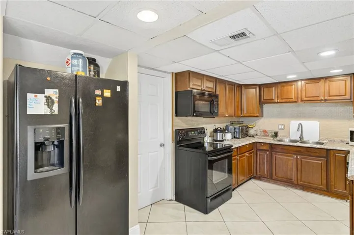 Kitchen with black appliances, brown cabinets, a paneled ceiling, light tile patterned floors, and backsplash