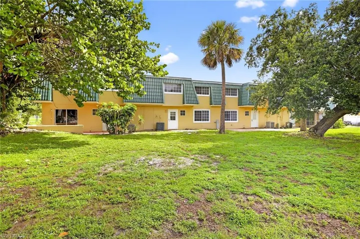 Rear view of property featuring stucco siding, mansard roof, and a lawn