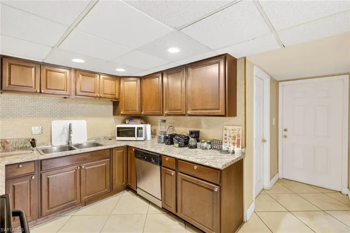 Kitchen featuring light tile patterned floors, dishwasher, brown cabinetry, backsplash, and a paneled ceiling