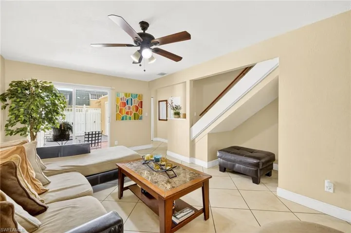 Living area with a ceiling fan, stairs, and light tile patterned flooring
