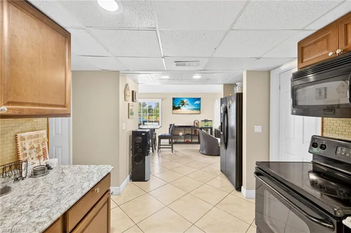 Kitchen featuring black appliances, a paneled ceiling, tasteful backsplash, light tile patterned floors, and brown cabinets