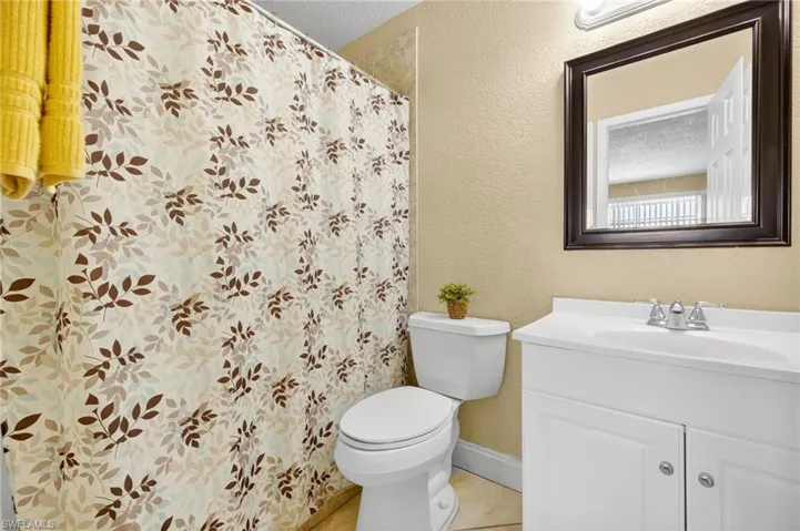 Full bathroom with vanity, tile patterned floors, a textured wall, and a shower with shower curtain