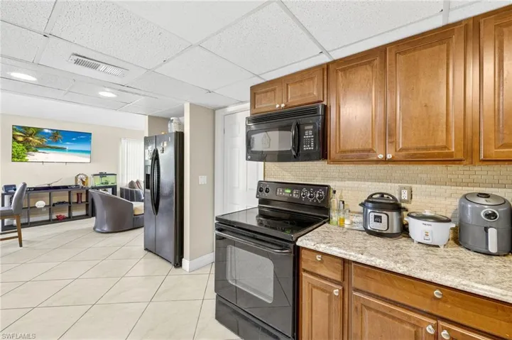Kitchen featuring black appliances, brown cabinets, tasteful backsplash, and a paneled ceiling