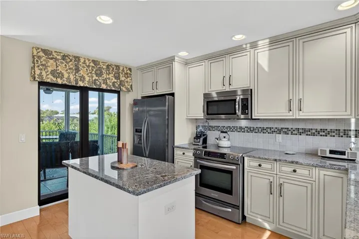 Kitchen featuring dark stone counters, appliances with stainless steel finishes, decorative backsplash, recessed lighting, and a center island