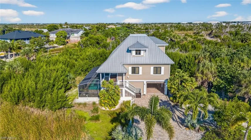 Back of house featuring a sunroom, a lanai, stairway, a metal roof, and driveway