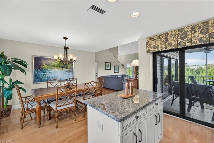 Kitchen with dark stone counters, hanging light fixtures, white cabinetry, a kitchen island, and light wood-style flooring