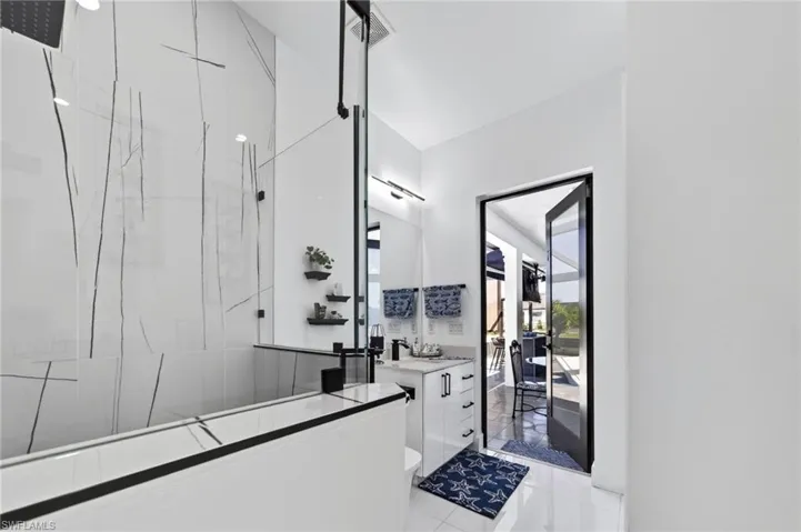 Modern 2-bedroom, bathroom featuring a glass-enclosed shower with large format tile, a rain shower head, and a sleek black framed vanity mirror, with pool access